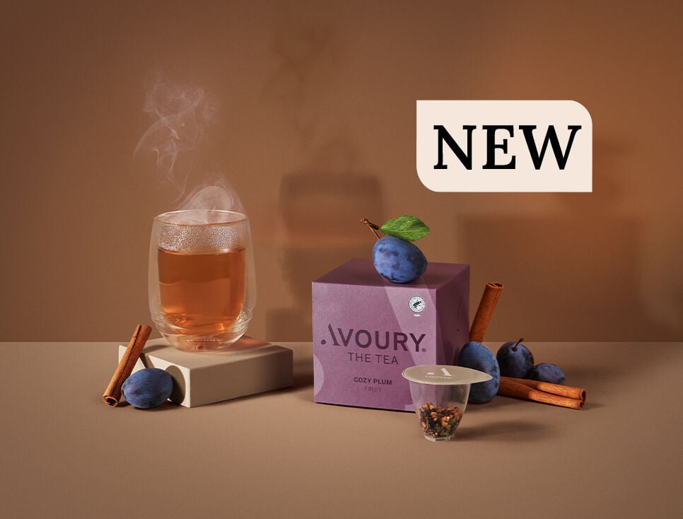 Plums, cinnamon a glass of steaming tea, a tea capsule, and a plum tea box